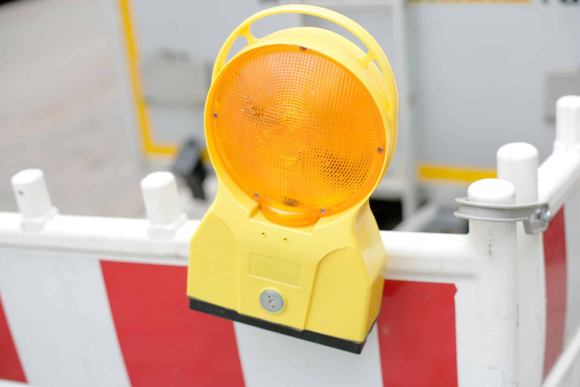 Gelbe Warnleuchte mit Blinklicht an rot-weisser Baustellenabsperrung – typisches Element zur Baustellenabsicherung im Strassenraum.